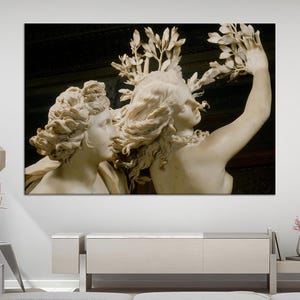 Può includere: Una scultura in marmo raffigurante due figure classiche con capelli ricci dettagliati e abiti fluenti. Una figura tiene un ramo frondoso sopra la testa. L'opera d'arte è ambientata su uno sfondo scuro, creando un contrasto con la pietra chiara.