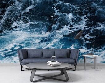 May include: A living room interior design featuring a blue and white ocean wave patterned wallpaper, a dark grey sofa, a grey coffee table, a black lamp on a white side table, and a white floor.