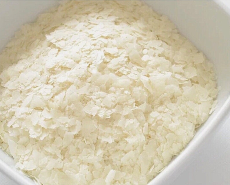 Op de afbeelding: Een close-up van een witte kom gevuld met kleine, witte vlokken gedroogde kokosnoot.