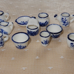 Könnte beinhalten: Eine Sammlung miniaturer weißer Porzellanstücke mit blauen Blumen- und Windmühlendesigns. Das Set umfasst Krüge, Schalen, eine Gießkanne und einen kleinen Korb, alle in einem klassischen blau-weißen Farbschema.