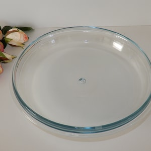 Könnte beinhalten: Eine klare Glas-Tortenform mit leicht erhöhtem Rand. Die Form ist leer und bereit zum Backen.