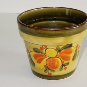 Könnte beinhalten: Ein gelber Keramik-Blumentopf mit grünem Rand und einem bemalten Blumendesign in Orange-, Gelb- und Grüntönen.