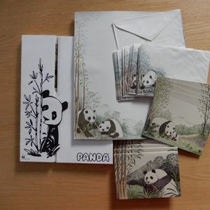 Könnte beinhalten: Ein Set an Pandabären-Briefpapier mit Schwarz-Weiß-Illustrationen von Pandabären auf weißem Hintergrund mit grünem Bambus und Blattwerk. Das Set enthält Umschläge, Briefpapier und Notizblöcke. Das Wort "PANDA" ist auf der Vorderseite des Briefpapiers gedruckt.