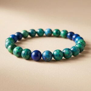 May include: A beaded bracelet featuring a strand of round, polished beads in shades of blue and green. The beads vary in color, with some displaying a speckled pattern. The bracelet is displayed on a neutral background.