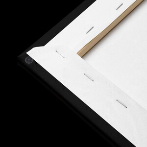 May include: Close-up of a stretched canvas art piece. The canvas is white and stapled to a wooden frame. The edges are black, and the corner is visible, showing the construction and texture of the artwork.