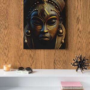 May include: A canvas print featuring a stylized African mask with intricate gold and black details. The mask has a serene expression and is adorned with geometric patterns. The artwork is displayed on a wooden wall, creating a striking contrast.