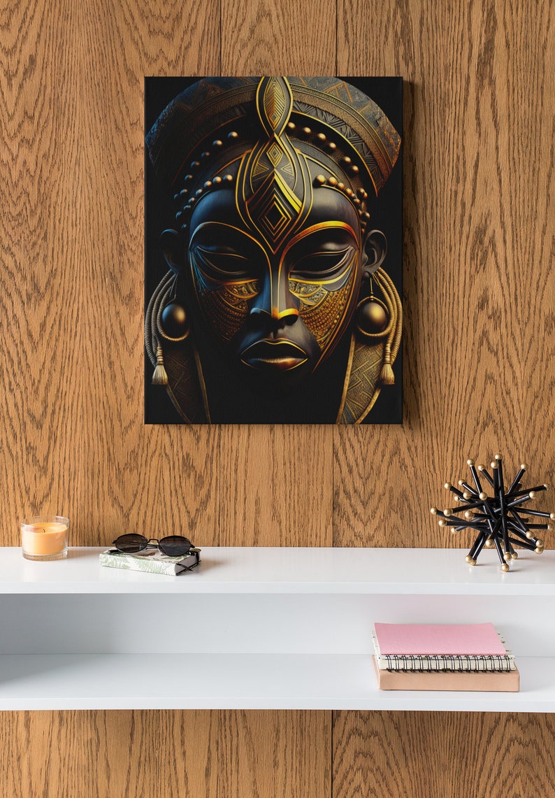 May include: A canvas print featuring a stylized African mask with intricate gold and black details. The mask has a serene expression and is adorned with geometric patterns. The artwork is displayed on a wooden wall, creating a striking contrast.