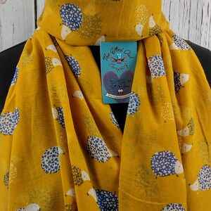 May include: A yellow scarf with a blue and white hedgehog print. The scarf has a tag that says "The Gifted Owl Company" and "Twist Twigs & Gifts for You".