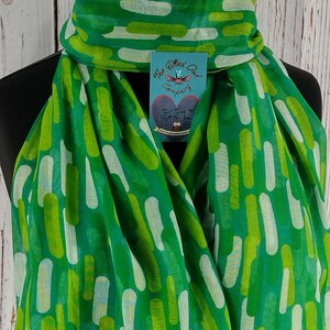 May include: A green scarf with a white and green abstract pattern. The scarf is folded and draped over a mannequin. A tag with the text "The Gifted Owl Company" is attached to the scarf.