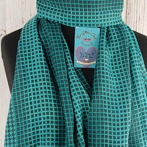 May include: A teal blue and black checkered scarf with a small tag that reads "The Gifted Owl Company" and "Twist Twice & Gift for You".