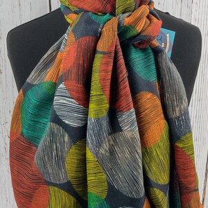 May include: A black scarf with a colourful abstract pattern of circles. The circles are outlined in yellow, orange, green, and red. The scarf is made of a soft, lightweight fabric.