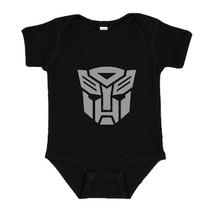 Könnte beinhalten: Schwarzer Baby-Strampler mit einem grauen Transformers-Logo auf der Vorderseite.