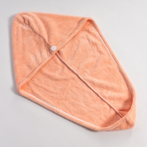 Peut inclure: Une serviette de cheveux à capuche pêche, faite d'un matériau doux et absorbant. La serviette a une fermeture à bouton à l'avant et une bordure blanche le long des bords. La serviette est conçue pour envelopper la tête et fixer les cheveux.
