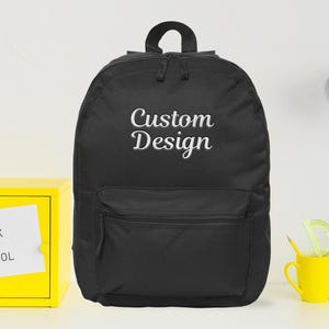 May include: Black backpack with the text "Custom Design" embroidered in white. The backpack has a front pocket and a top handle. A yellow box with "Back to School" text is on the left.