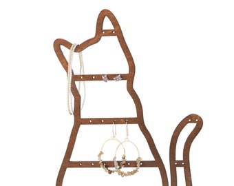 Pode incluir: Um organizador de joias em forma de gato de madeira com acabamento castanho escuro. O organizador tem vários orifícios para brincos e espaço para colares. A cauda do gato curva-se para cima. A base tem a palavra "Wrenn" impressa.
