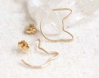 Pode incluir: Um par de brincos de argola de ouro em forma de gato. Os brincos são feitos de fio fino e têm um design simples e minimalista.
