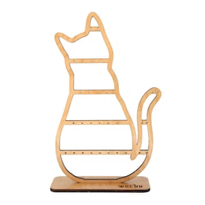 May include: A wooden cat-shaped jewelry organizer. The light brown organizer has multiple rows of small holes for earrings and a base with the word "WRENN" printed on it. The cat's tail is curved.