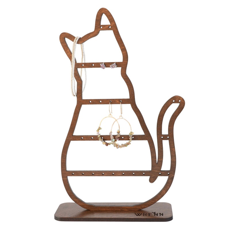 May include: A wooden cat-shaped jewelry organizer in a dark brown finish. The organizer has multiple holes for earrings and a space for necklaces. The cat's tail curves upwards. The base has the word "Wrenn" printed on it.
