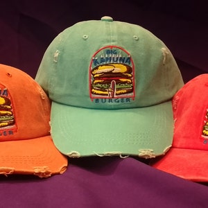 Puede incluir: Tres gorras de béisbol desgastadas en naranja, verde azulado y rojo. Cada gorra presenta un diseño bordado de "Big Kahuna Burger". Las gorras tienen un aspecto desgastado con bordes deshilachados, lo que sugiere un estilo vintage o casual.