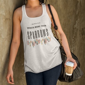 May include: White tank top with the text "Matthew 10:31 WORTH MORE THAN SPARROWS" and a row of colorful feathers printed on the front.