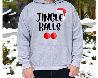 May include: A light gray hooded sweatshirt with the text "JINGLE BALLS" in black. The design includes a Santa hat and two red Christmas ornaments. The person is wearing blue jeans.