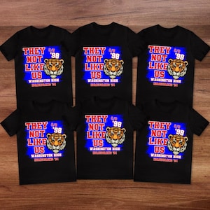 May include: Black t-shirts with a tiger graphic and the text "THEY NOT LIKE US" in red and blue. The text "WASHINGTON HIGH HOMECOMING '98" is also printed on the shirts. The shirts are short-sleeved.