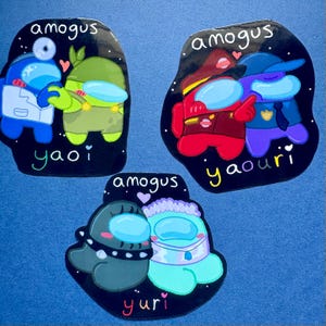以下が含まれることがあります： 宇宙服を着た漫画のキャラクターが描かれた3枚の光沢のあるステッカー。左上は青と緑のペアで「amogus yaoi」の文字。右上は赤と紫のキャラクターで「amogus yaouri」。下は黒とターコイズのキャラクターで「amogus yuri」と書かれています。