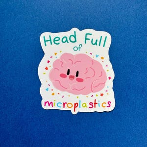 May include: A sticker with a pink cartoon brain with a smiling face. The sticker has the words "Head Full of" above the brain and "microplastics" below it, all in colorful text. The background is blue.