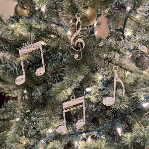 May include: A Christmas tree decorated with music note ornaments. The ornaments are made of paper and feature musical notation. The tree is also decorated with gold ornaments and white lights.