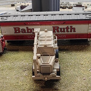 May include: A white toy military vehicle with a black grill and a red and white boxcar behind it. The boxcar has the words "Baby Ruth" printed on the side.