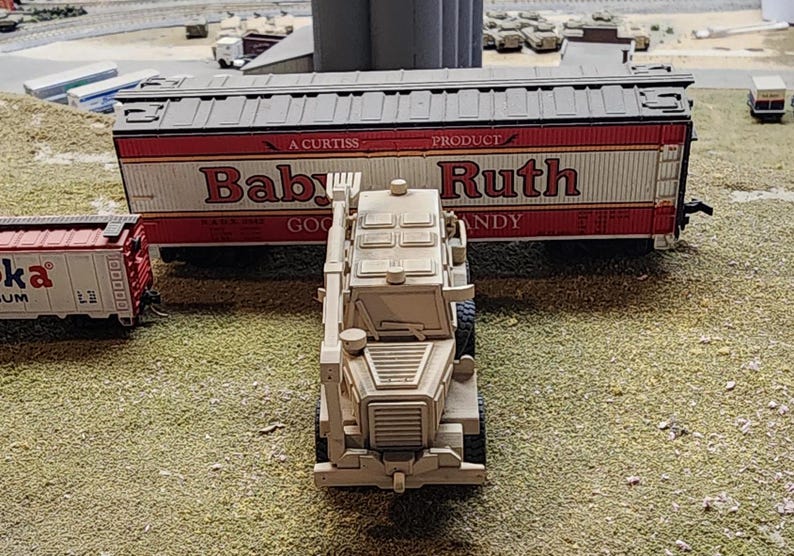 May include: A white toy military vehicle with a black grill and a red and white boxcar behind it. The boxcar has the words "Baby Ruth" printed on the side.