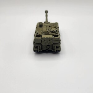 May include: A green toy military tank with a raised cannon. The tank is on a white background.
