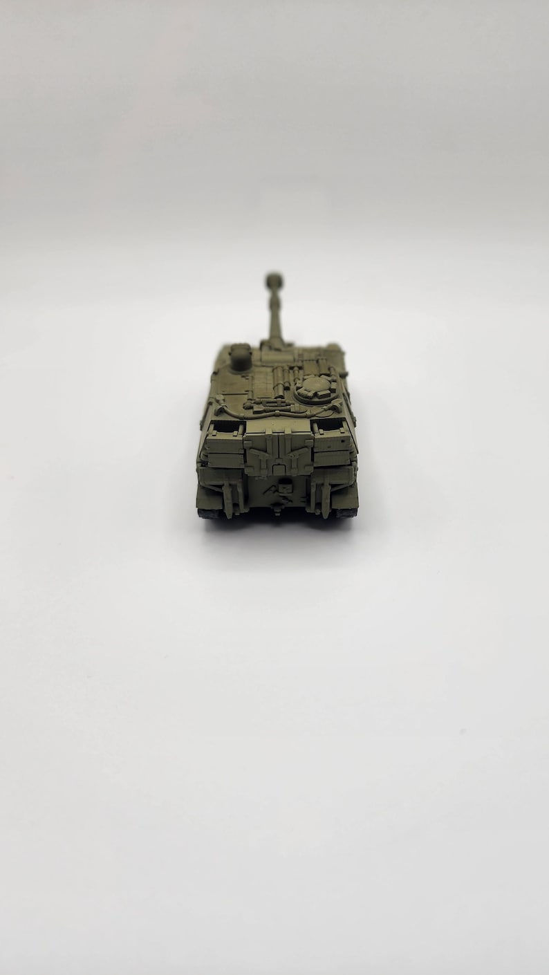 May include: A green toy military tank with a raised cannon. The tank is on a white background.