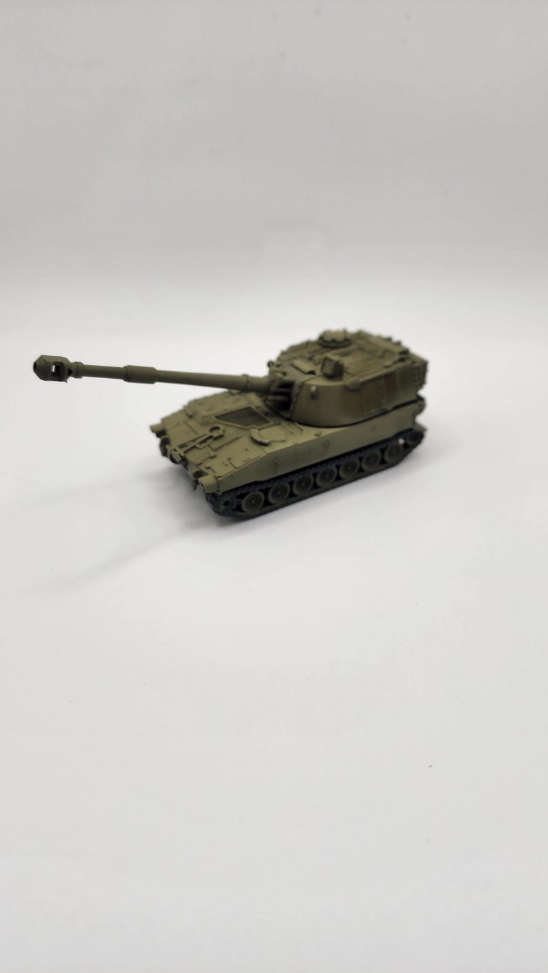 May include: A green toy model of a self-propelled howitzer artillery piece with a long barrel and a rotating turret.