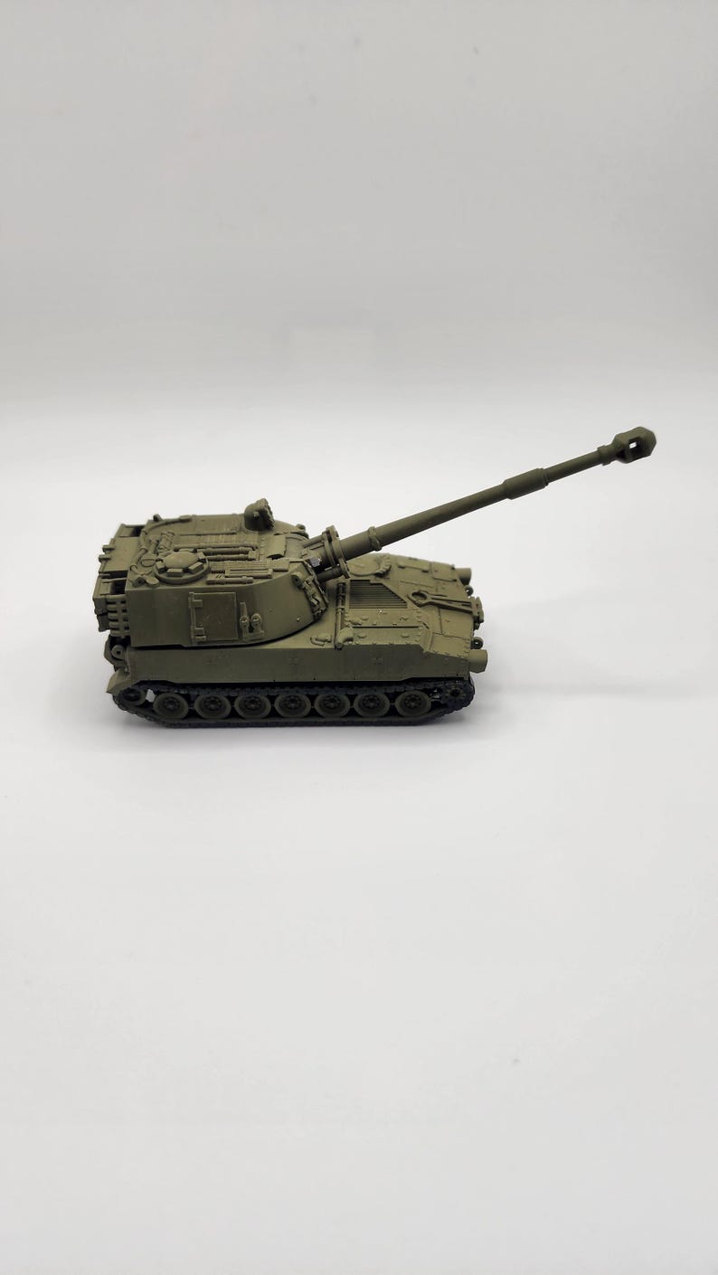 May include: A green toy model of a self-propelled howitzer artillery piece with a long barrel and a detailed design.