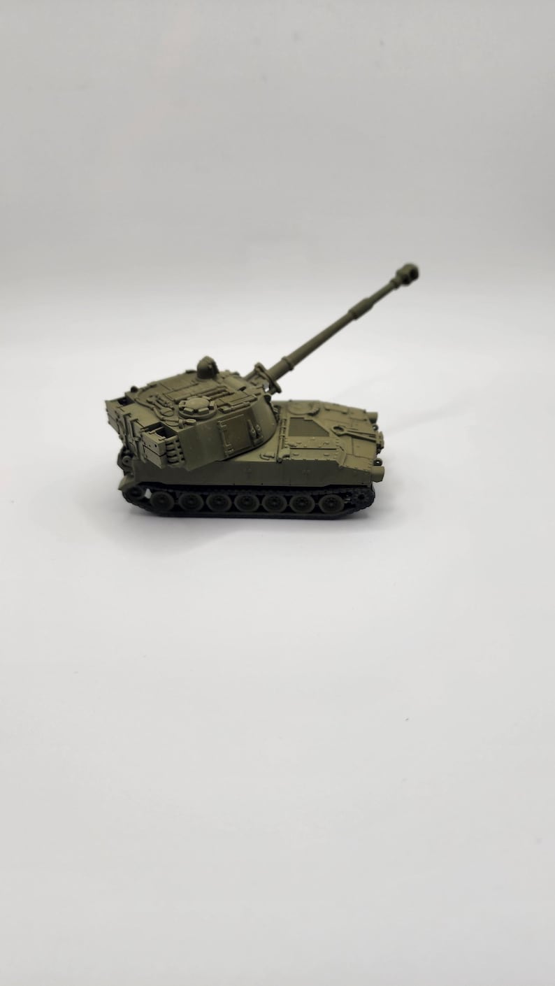May include: A green toy model of a self-propelled howitzer artillery piece with a long barrel and a rotating turret.