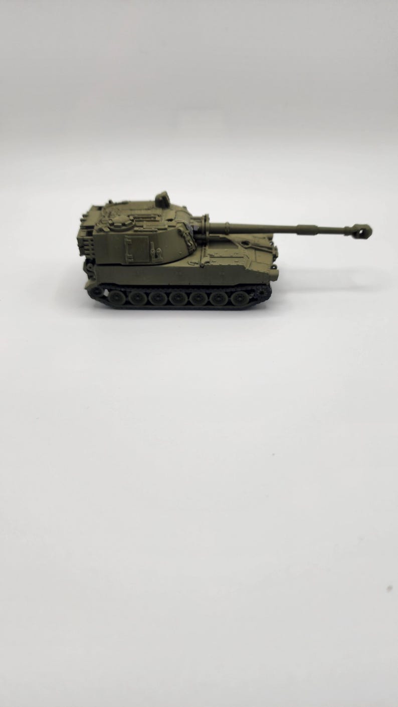 May include: A green toy model of a self-propelled howitzer, a type of artillery.