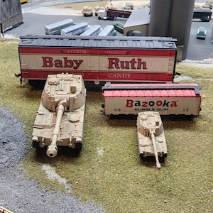 May include: A model train set with a red boxcar with the words "Baby Ruth Candy" on the side, a beige tank, and a smaller beige tank with a red boxcar with the words "Bazooka Bubble Gum" on the side.