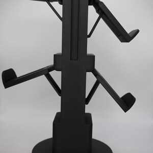 Pode incluir: Um suporte preto impresso em 3D com quatro bra&ccedil;os que podem ser ajustados para segurar v&aacute;rios dispositivos. O suporte tem uma base quadrada e uma base redonda.