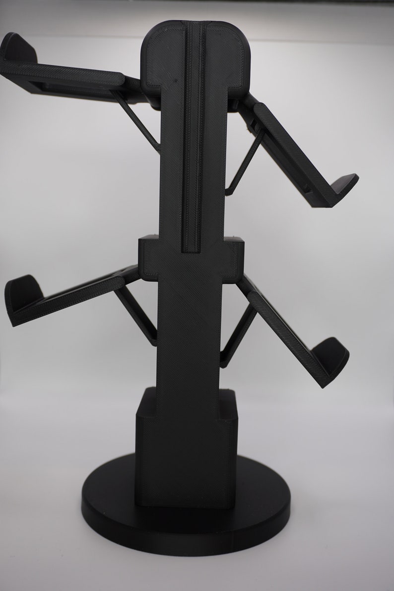 Pode incluir: Um suporte preto impresso em 3D com quatro bra&ccedil;os que podem ser ajustados para segurar v&aacute;rios dispositivos. O suporte tem uma base quadrada e uma base redonda.