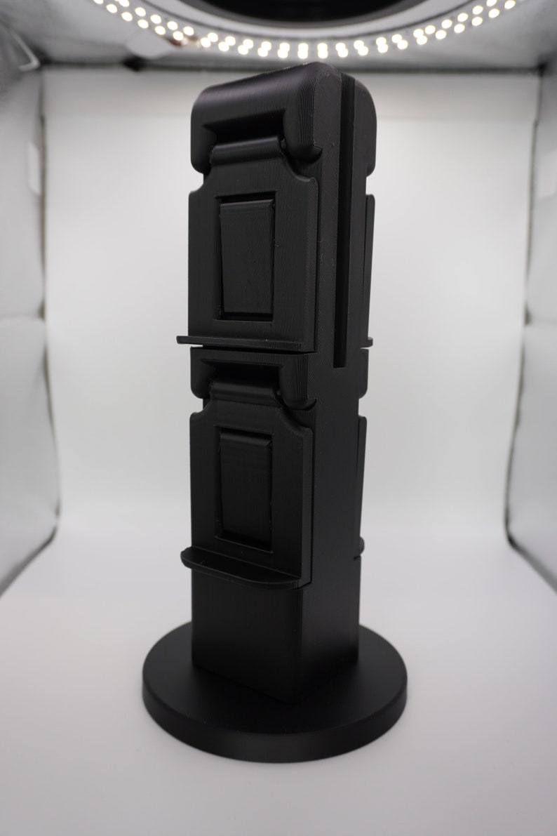 Pode incluir: Um suporte de telefone dobr&aacute;vel de tr&ecirc;s n&iacute;veis de cor preta com uma base redonda. O suporte &eacute; feito de pl&aacute;stico e tem um acabamento liso e fosco.