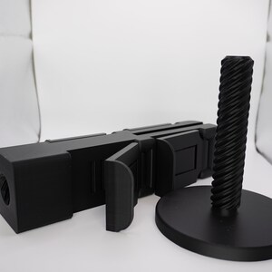 Pode incluir: Um objeto preto segmentado, articulado, impresso em 3D com uma base redonda e rosqueada preta. O objeto &eacute; projetado para ser usado como um suporte ou suporte.