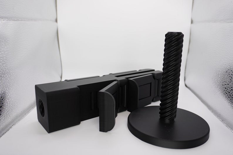 Pode incluir: Um objeto preto segmentado, articulado, impresso em 3D com uma base redonda e rosqueada preta. O objeto &eacute; projetado para ser usado como um suporte ou suporte.