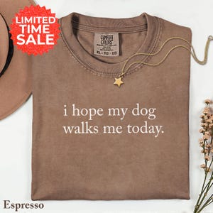 May include: Espresso-colored t-shirt with the text "i hope my dog walks me today." A gold star pendant necklace rests on the shirt. A red "LIMITED TIME SALE" sticker is in the upper left corner.