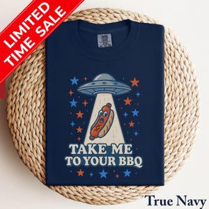 May include: True Navy t-shirt with a graphic of a UFO beaming up a hot dog, surrounded by stars. The text "TAKE ME TO YOUR BBQ" is below the graphic. A red banner in the upper left corner reads "LIMITED TIME SALE".