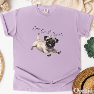 May include: A lavender t-shirt with a cartoon pug and the text "Live, Laugh, Snort."