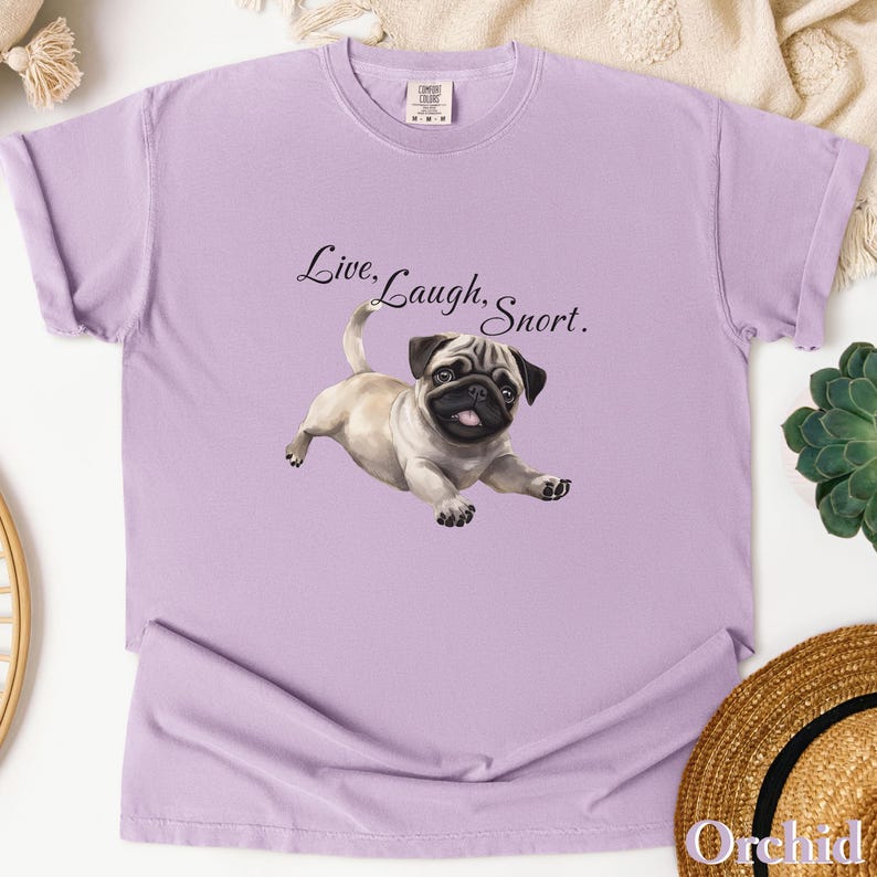 May include: A lavender t-shirt with a cartoon pug and the text "Live, Laugh, Snort."
