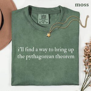 May include: A moss green crew neck t-shirt with the white text "i'll find a way to bring up the pythagorean theorem" printed on the front. The shirt features a Comfort Colors brand label at the inner neckline and is size XL.