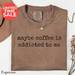 May include: Espresso-colored t-shirt with the phrase "maybe coffee is addicted to me" in black text. A gold star pendant necklace rests on the shirt. A "Limited Time Sale" sticker is in the upper left corner.