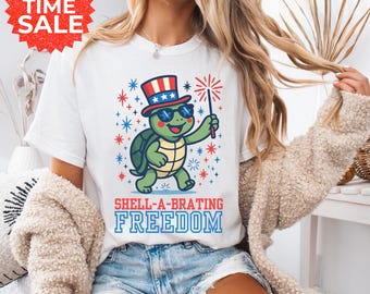 May include: White t-shirt with a cartoon turtle wearing sunglasses and a patriotic hat, holding a sparkler. The shirt has the text "SHELL-A-BRATING FREEDOM" in blue. A red and white "LIMITED TIME SALE" graphic is in the upper left corner.
